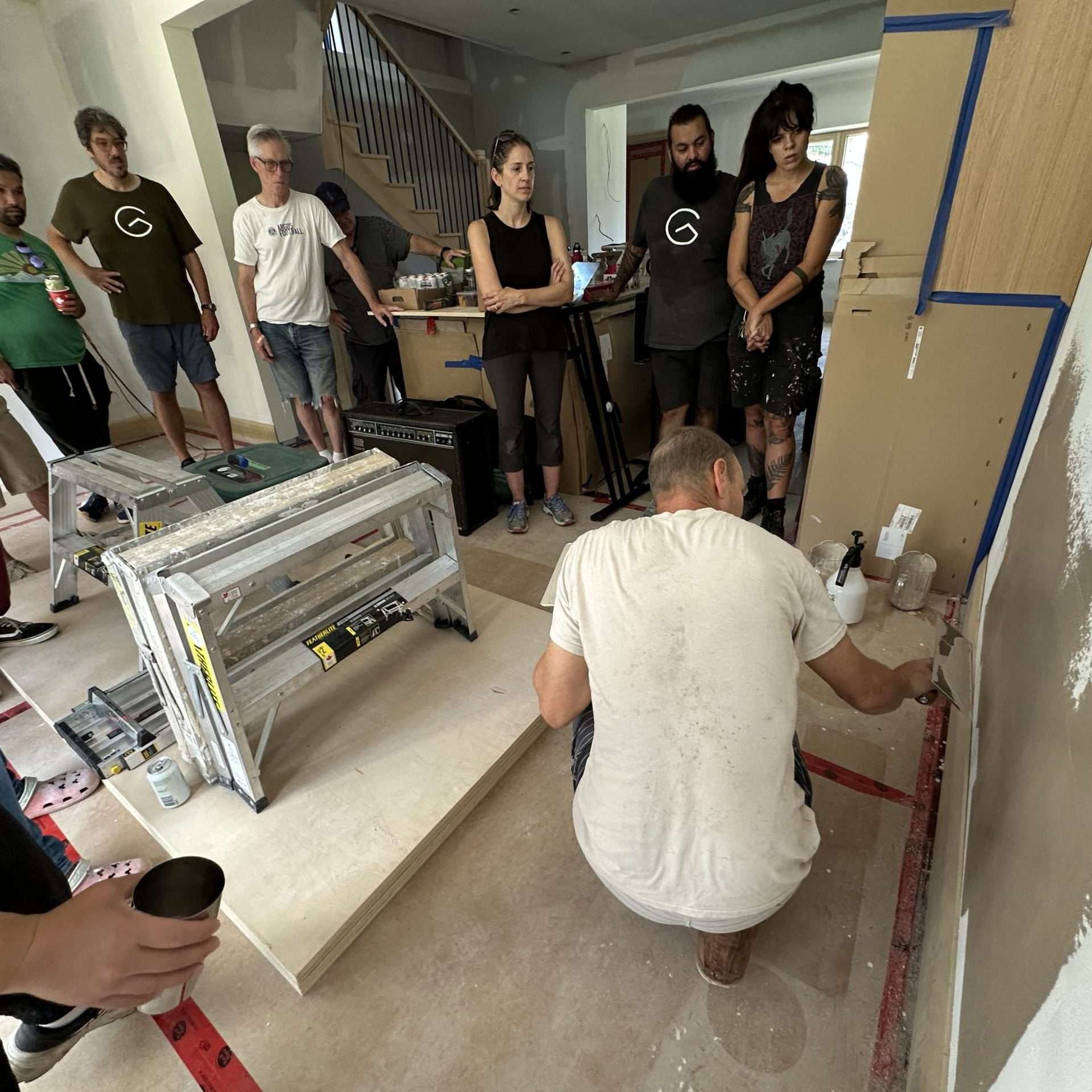 Home renovation workshop with group of people observing a craftsman working on wall.