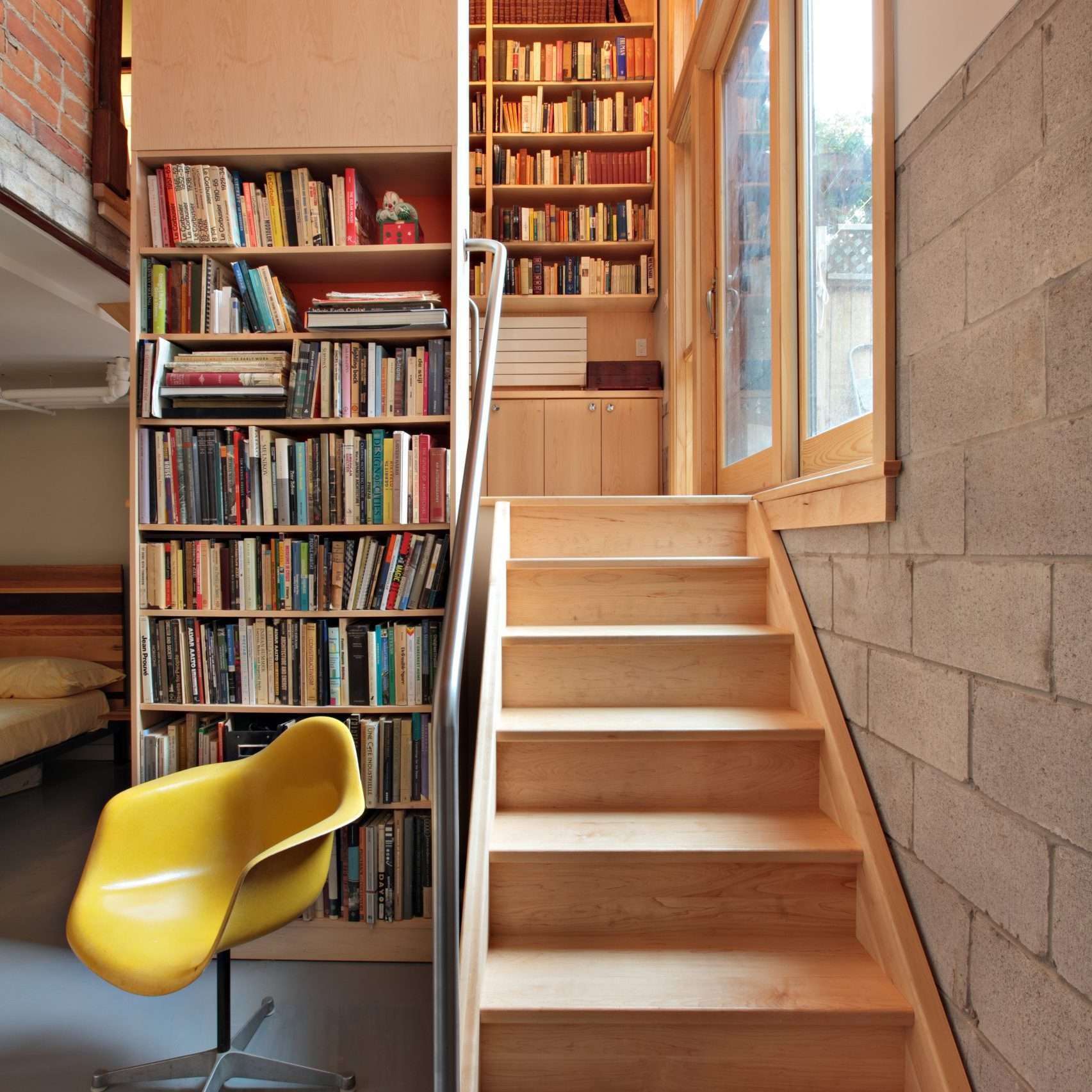 Bookshelf and staircase interior in a cozy home library, featuring wooden stairs and a yellow chair.